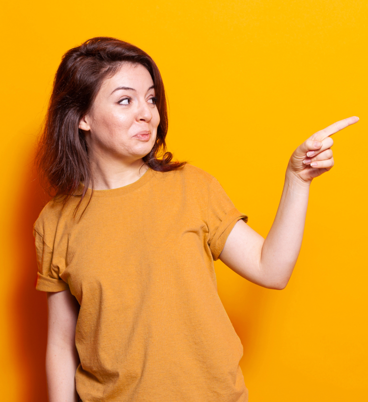Cheerful young woman in a mustard t-shirt pointing right with a playful expression on a vibrant yellow background — digital marketing concept.